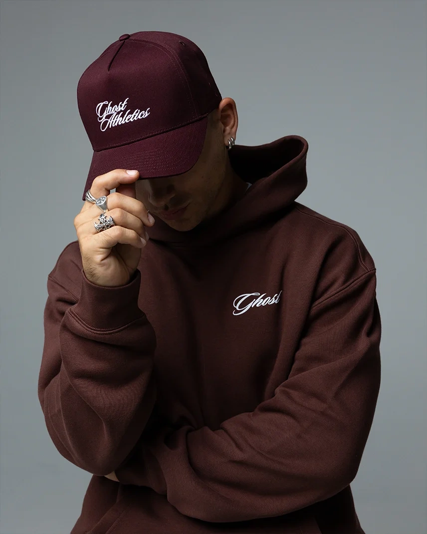 Model pulling down the maroon GHOST® ATHLETICS baseball hat