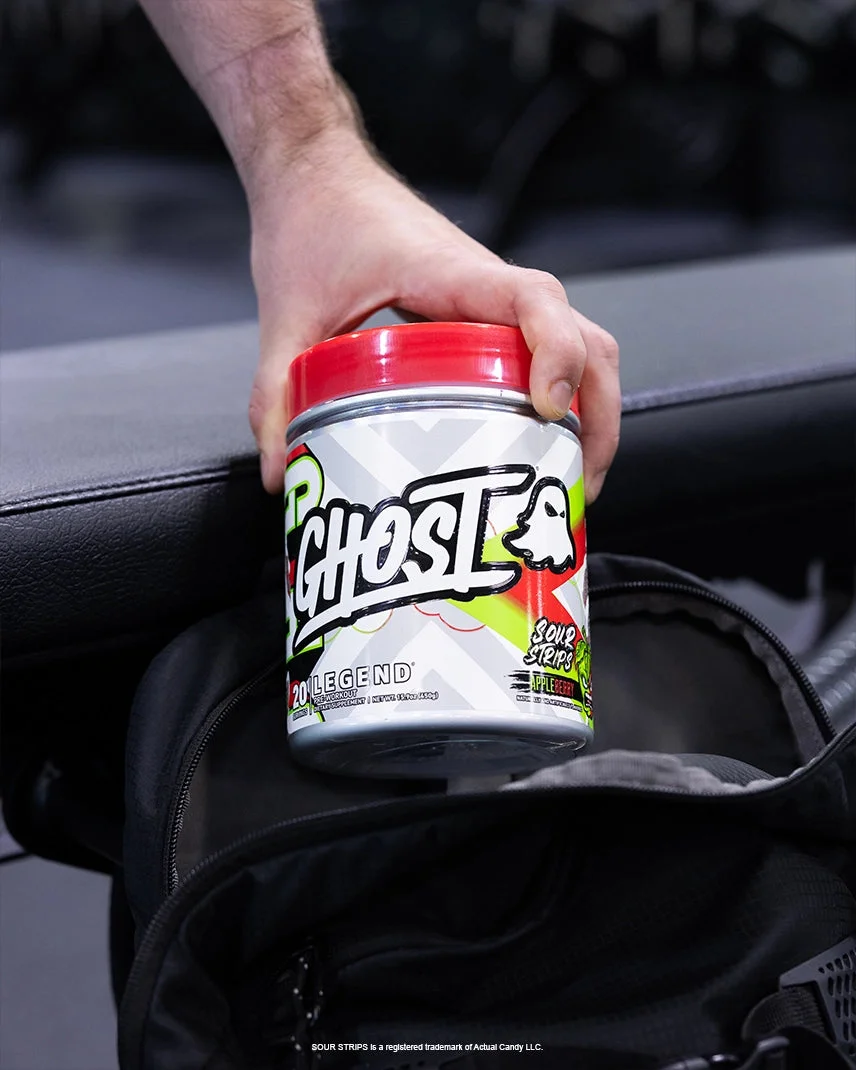 A hand dropping a tub of GHOST LEGEND® x SOUR STRIPS® Appleberry into a gym bag