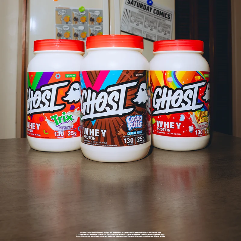 Three GHOST® WHEY tubs in cereal collab flavors on a wooden table
