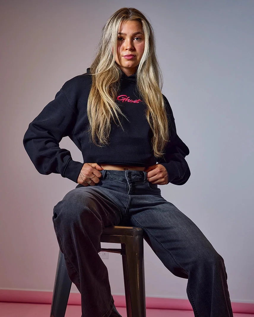 Model seated on a stool in the black GHOST® STRIDES hoodie