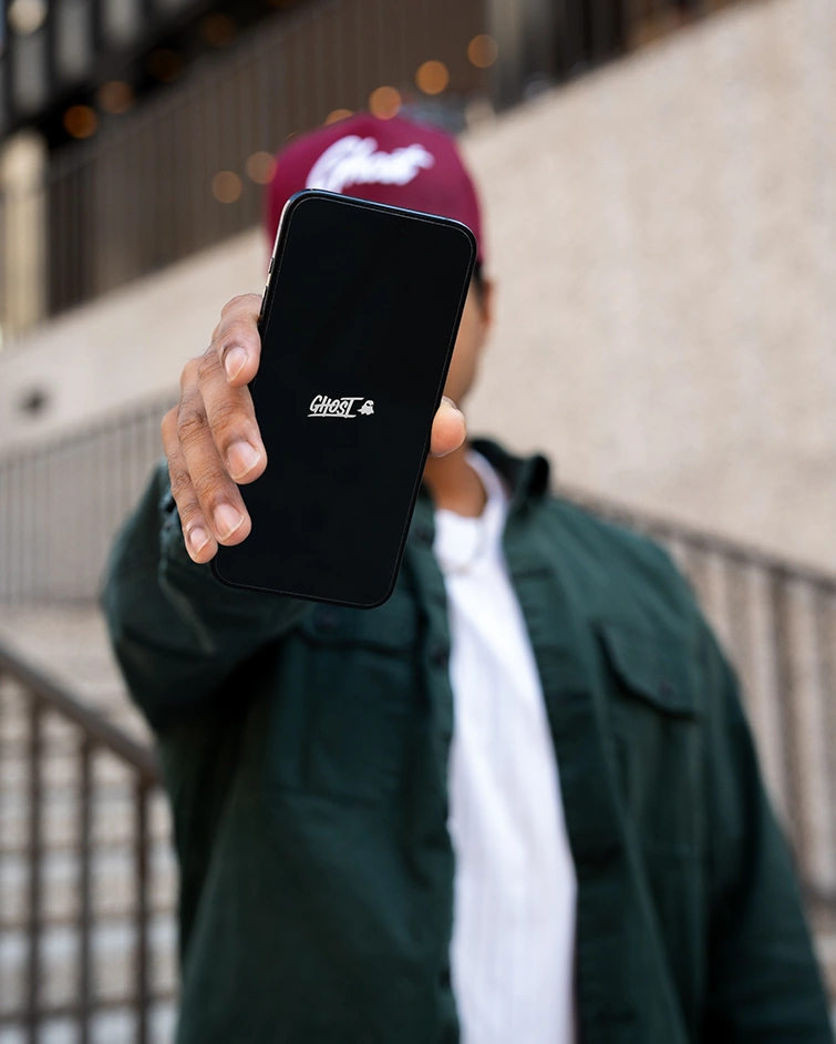 A hand holding up a phone showing the GHOST® app