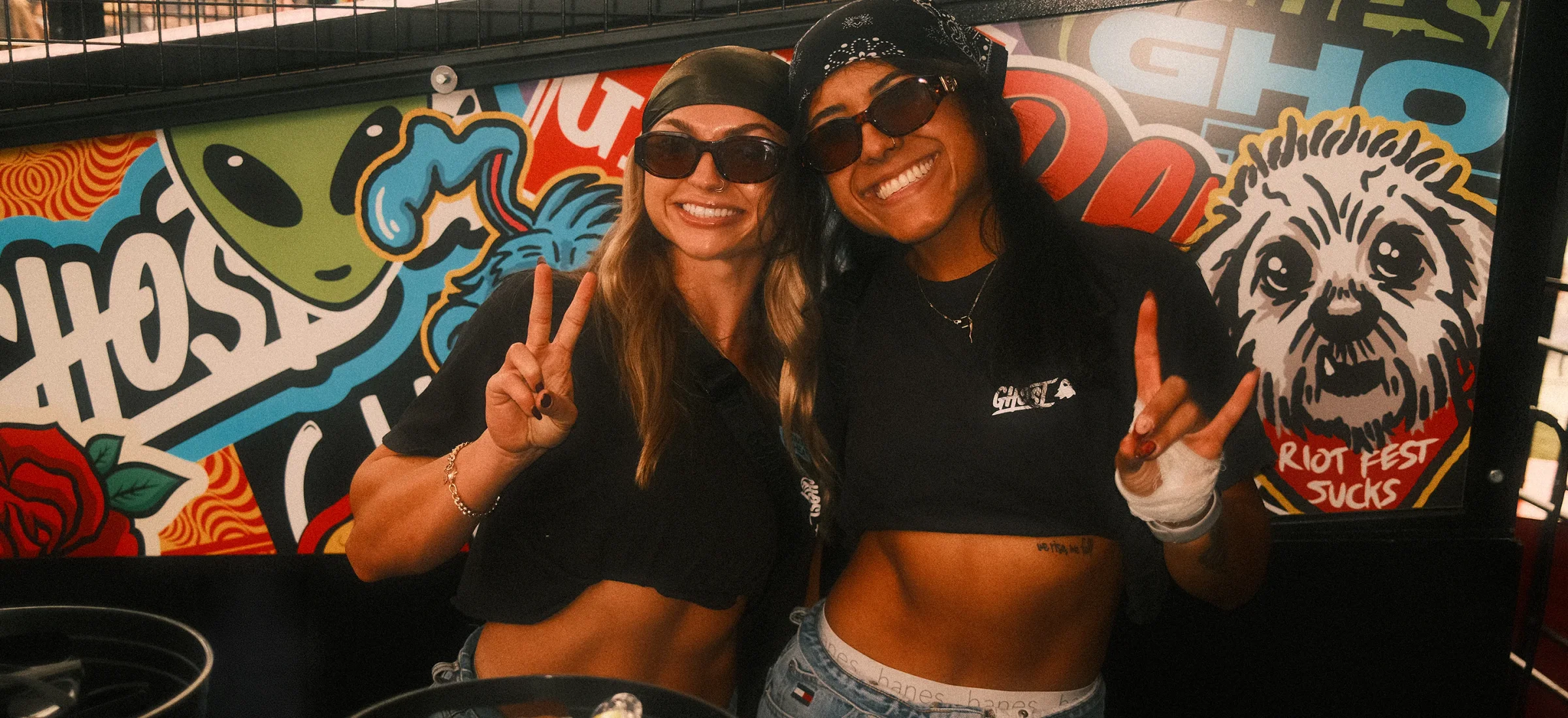 Two GHOST® Takeover Team members throwing peace signs in front of a graffiti GHOST® truck